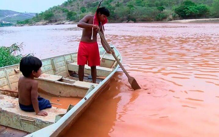 Members of Krenak people, father and son navigate on the turbid waters, completely contaminated, of the river Doce. Photo: Reproduction. 