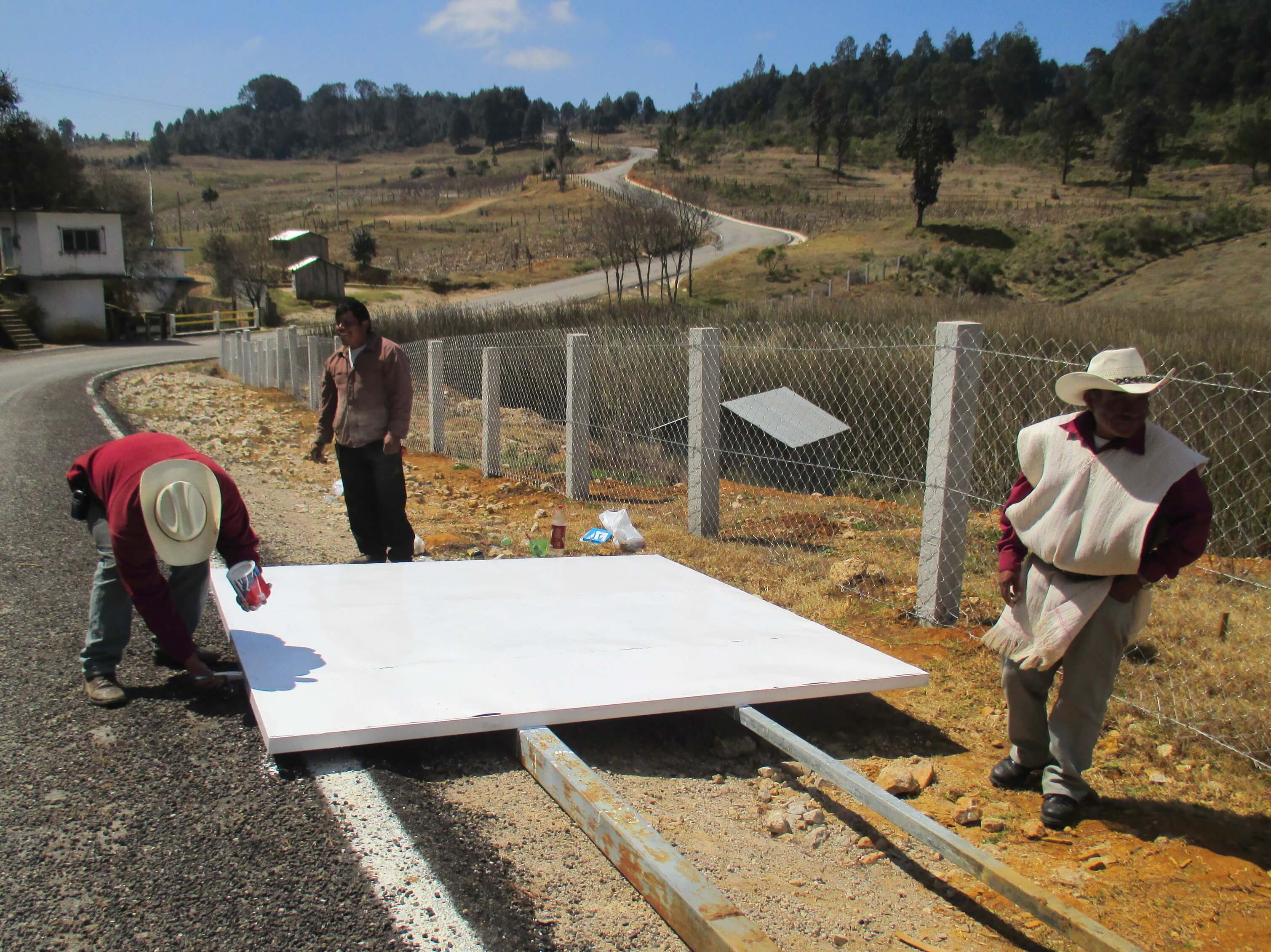 Candelaria residents paint over graffiti to fix up a roadside sign proclaiming their opposition to the highway project. (WNV/Sandra Cuffe)